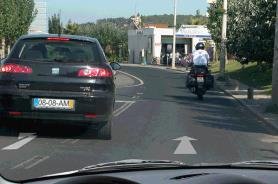 Dashcam view behind a black car with a motorcycle ahead on a town road